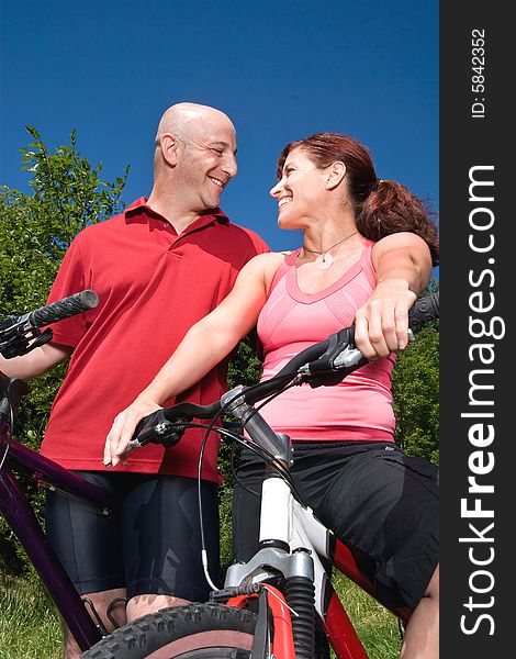 A young couple sits on bikes, on a sunny day, at a park, staring happily at each other. - vertically framed. A young couple sits on bikes, on a sunny day, at a park, staring happily at each other. - vertically framed