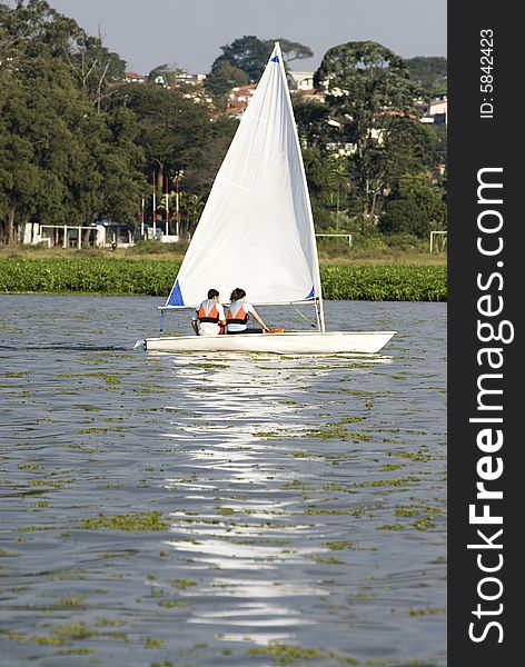 A young couple is sailing on a lake together.  They are looking away from the camera.  Vertically framed shot. A young couple is sailing on a lake together.  They are looking away from the camera.  Vertically framed shot.