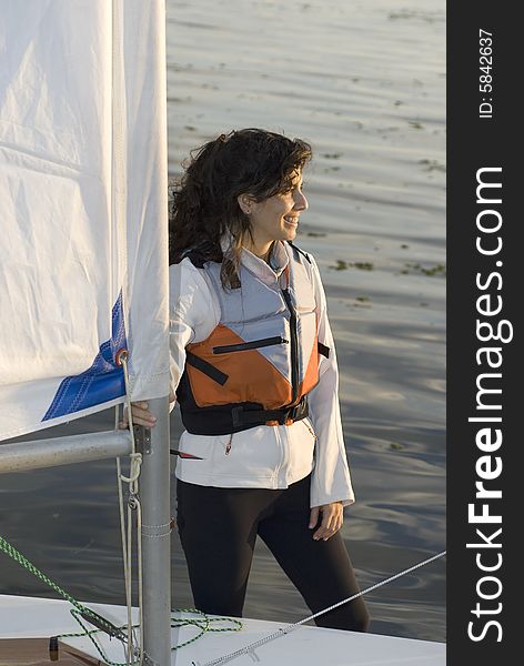 A young woman is standing in the water next to her sailboat.  She is holding onto the sail.  She is smiling and looking away from the camera.  Vertically framed shot. A young woman is standing in the water next to her sailboat.  She is holding onto the sail.  She is smiling and looking away from the camera.  Vertically framed shot.