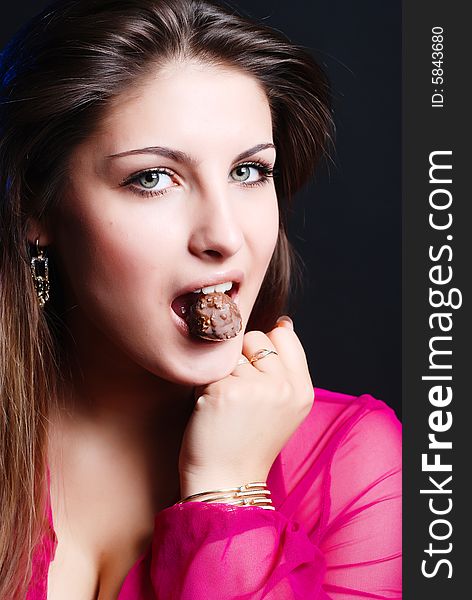 Portrait of beautiful girl in a pink woman's jacket with a chocolate candy in the mouth