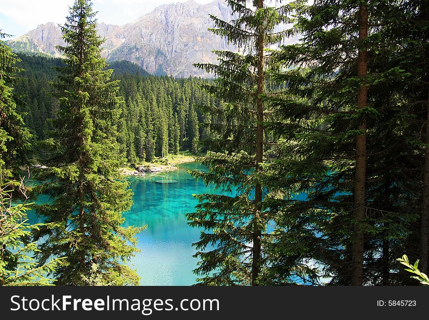 Sella montain group, and Carezza lake's turquoise colorful water.  Green pines forest on blue lake water. Italy. Sella montain group, and Carezza lake's turquoise colorful water.  Green pines forest on blue lake water. Italy