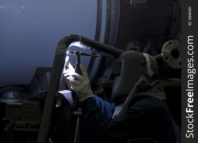 Welder working on steel pipes in an industrial workshop. dark, contrasty photo.