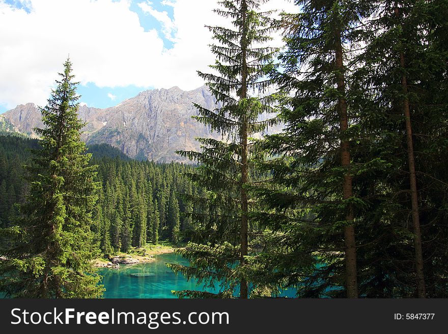 Green pines woods, blue turqoise Carezza  lake & view on Sella montain group, Italy. Green pines woods, blue turqoise Carezza  lake & view on Sella montain group, Italy