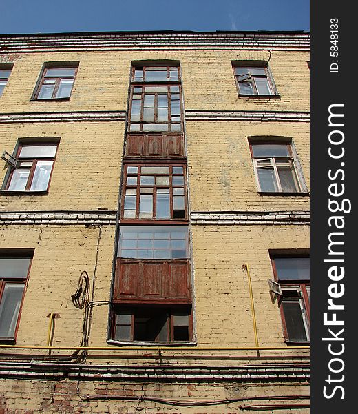 The old multi-storey apartment house from a brick is painted light yellow color with greater glass windows on a background of the dark blue sky. The old multi-storey apartment house from a brick is painted light yellow color with greater glass windows on a background of the dark blue sky