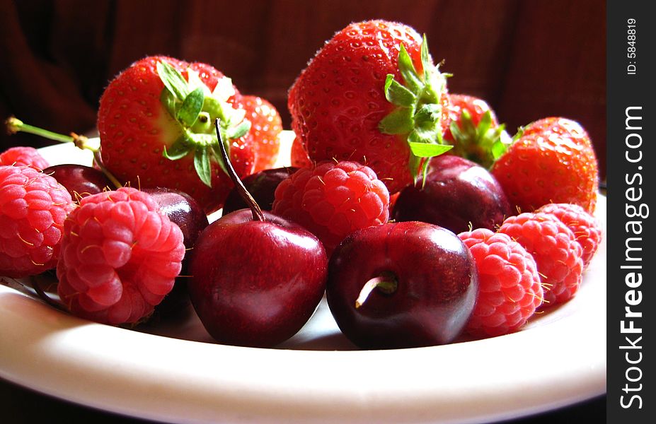 A white plate of red summer fruits - strawberries, cherries and raspberries. A white plate of red summer fruits - strawberries, cherries and raspberries.