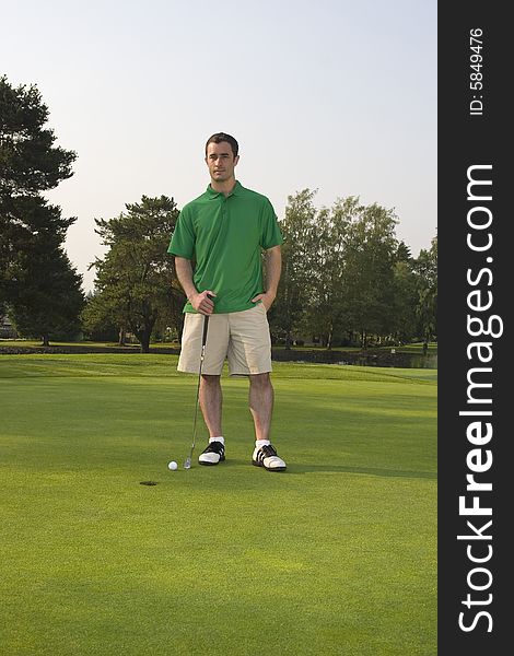 Male golfer casually standing on green holding golf club. Vertically framed shot. Male golfer casually standing on green holding golf club. Vertically framed shot.