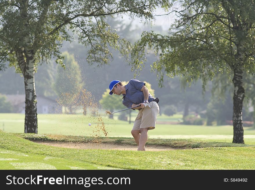 Man hitting golf ball out of sand trap - horizontally framed photo. Man hitting golf ball out of sand trap - horizontally framed photo.