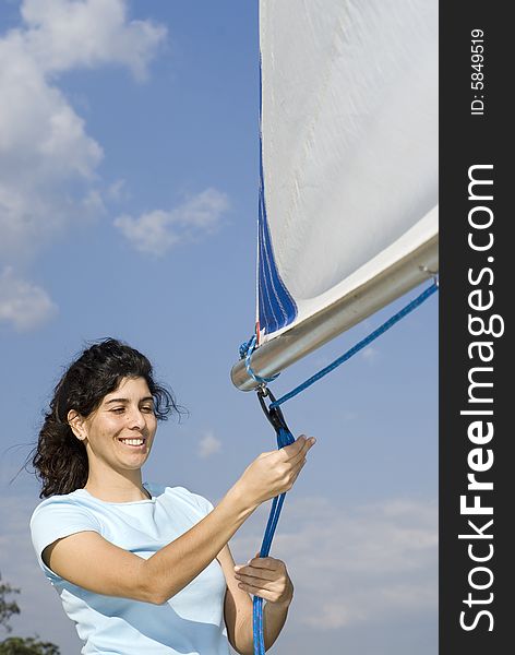 Woman standing next to sailboat tying rigging to sail. Vertically framed photo. Woman standing next to sailboat tying rigging to sail. Vertically framed photo