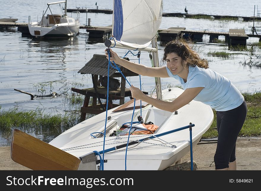 Woman standing next to sailboat setting rigging on sails. Looking at camera. Horizontally framed photo. Woman standing next to sailboat setting rigging on sails. Looking at camera. Horizontally framed photo