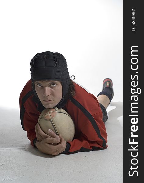 A young man, lies on the ground, holding a rugby ball, looking serious. Vertically framed shot. A young man, lies on the ground, holding a rugby ball, looking serious. Vertically framed shot.