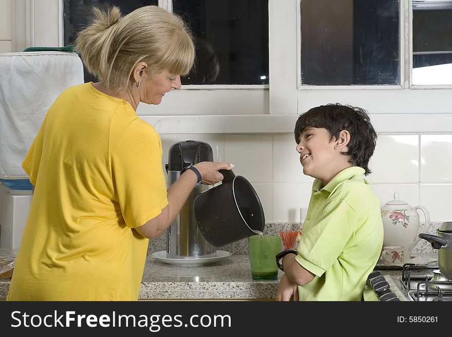 Woman and boy standing in kitchen. Woman pouring boy drink. Boy smiling at woman. Horizontally framed photo. Woman and boy standing in kitchen. Woman pouring boy drink. Boy smiling at woman. Horizontally framed photo.