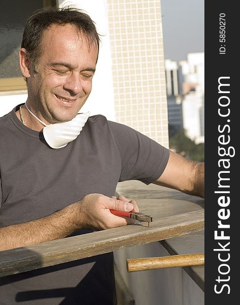 Man pulling nail with pliers. He is smiling and looking at the nail. He has a mask around his neck. Vertically framed shot. Man pulling nail with pliers. He is smiling and looking at the nail. He has a mask around his neck. Vertically framed shot.