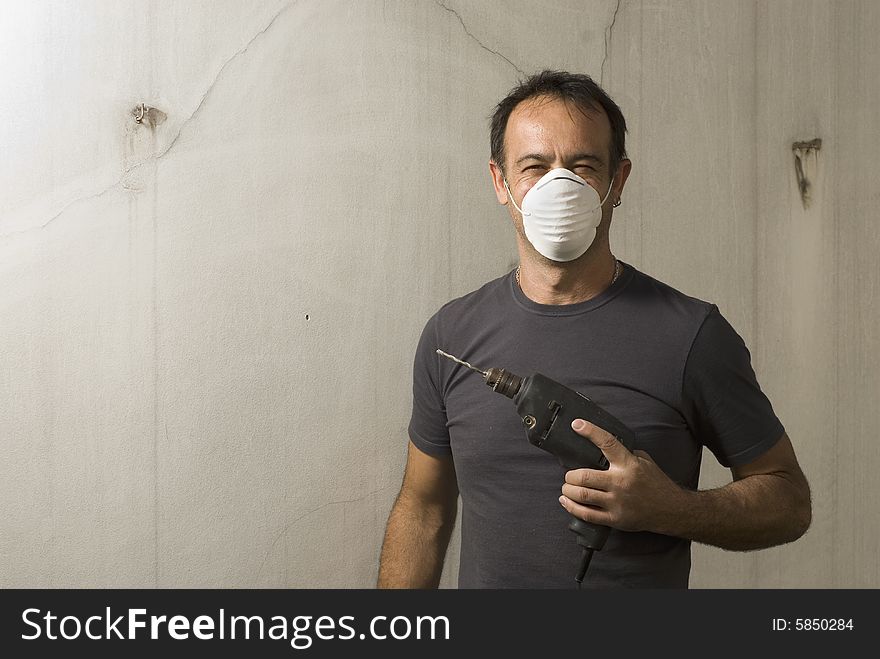 Man standing while holding drill. He is wearing a mask and smiling. He is looking at cameral. Horizontally framed shot. Man standing while holding drill. He is wearing a mask and smiling. He is looking at cameral. Horizontally framed shot.