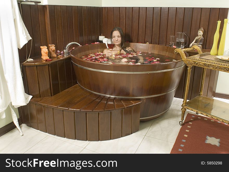 Attractive woman relaxing in a hot tub with a glass of wine while surrounded by flower petals. Horizontally framed shot. Attractive woman relaxing in a hot tub with a glass of wine while surrounded by flower petals. Horizontally framed shot.