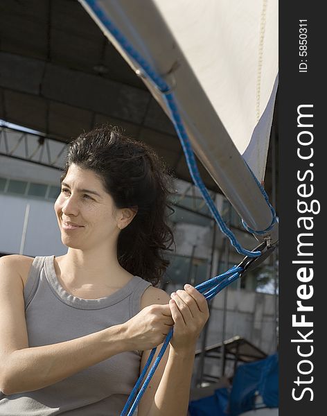 Woman standing next to sailboat smiling away from camera and holding sail rigging. Vertically framed photo. Woman standing next to sailboat smiling away from camera and holding sail rigging. Vertically framed photo.