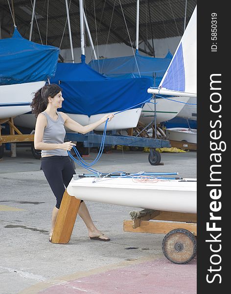 Woman standing behind sailboat on trailer. Tightening sail rigging. Vertically framed photo. Woman standing behind sailboat on trailer. Tightening sail rigging. Vertically framed photo