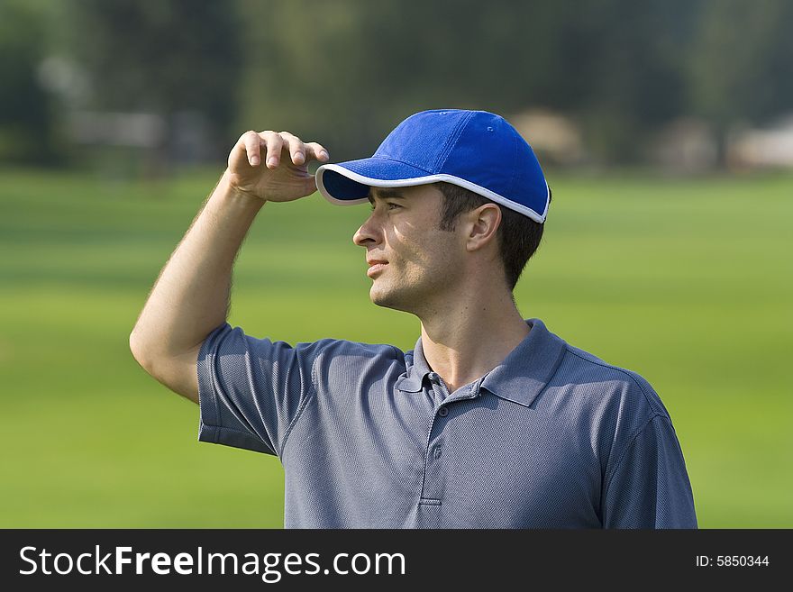 Man's profile while standing on golf course shielding eyes from sun - Horizontally framed photo. Man's profile while standing on golf course shielding eyes from sun - Horizontally framed photo