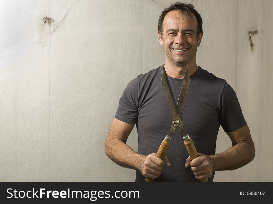 Man standing smiling at camera holding pair of garden shears. Horizontally framed shot. Man standing smiling at camera holding pair of garden shears. Horizontally framed shot.