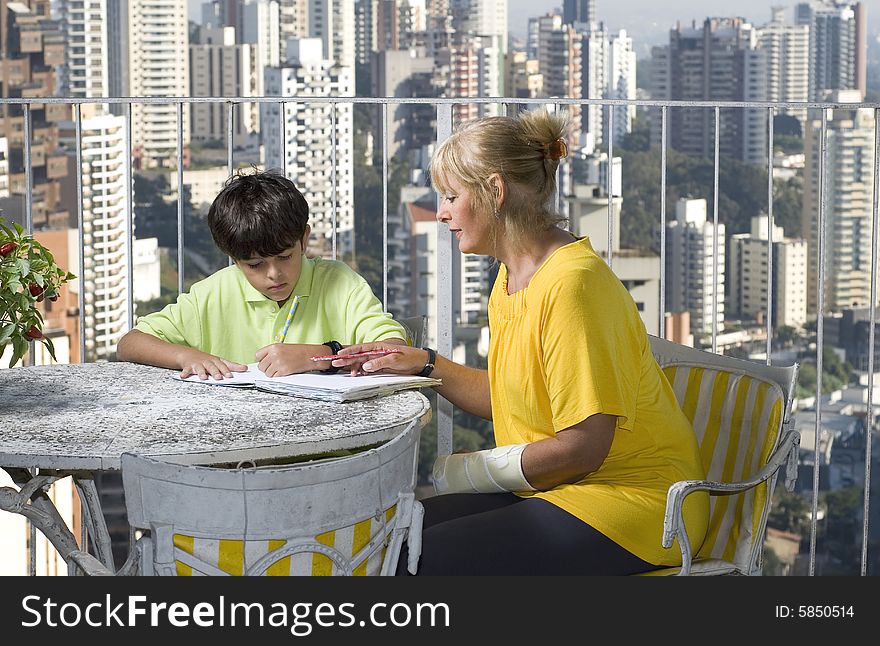 Woman watching or helping boy write. Woman and boy sitting on balcony overlooking city. Horizontally framed photo. Woman watching or helping boy write. Woman and boy sitting on balcony overlooking city. Horizontally framed photo.