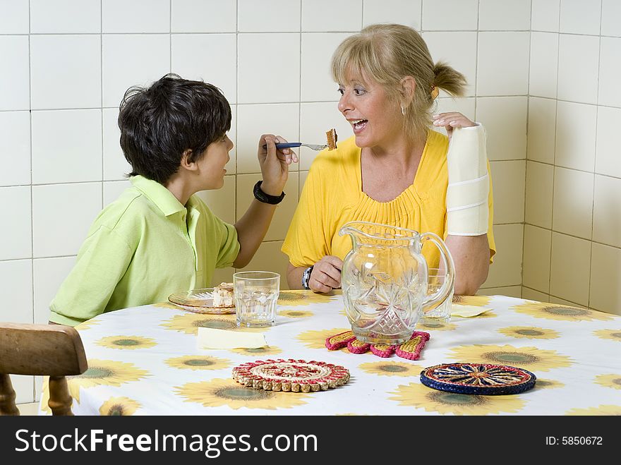 Boy and woman sitting at table. Boy feeding woman. Woman wearing cast. Horizontally framed photo. Boy and woman sitting at table. Boy feeding woman. Woman wearing cast. Horizontally framed photo.