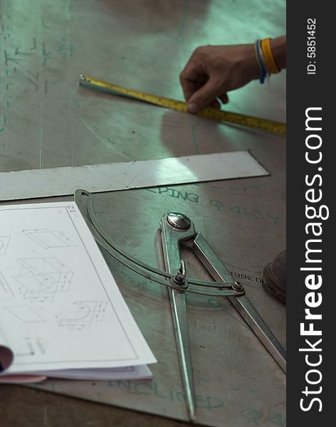 Design being done on a factory floor with compass and construction plans. Shallow depth of field with compass in focus. Design being done on a factory floor with compass and construction plans. Shallow depth of field with compass in focus.