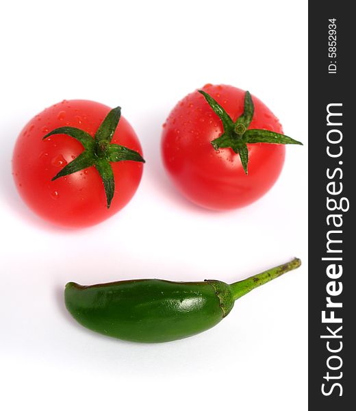 Green chili with cherry tomatoes forming a face on white background. Green chili with cherry tomatoes forming a face on white background