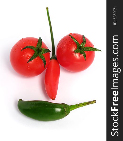 Two colors chilies with cherry tomatoes forming a face on white background. Two colors chilies with cherry tomatoes forming a face on white background