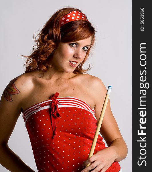 Redhead holding a pool cue stick, wearing a red polka dot outfit with. White background. Redhead holding a pool cue stick, wearing a red polka dot outfit with. White background