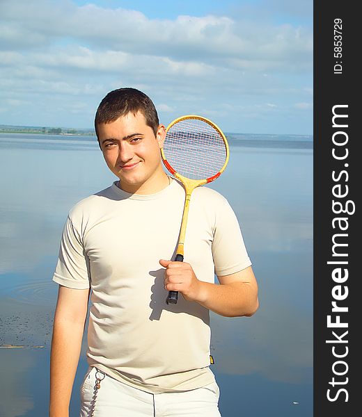 Young man with a racket for a badminton on the riverside.  Sport and rest. Healthy life. Young man with a racket for a badminton on the riverside.  Sport and rest. Healthy life.