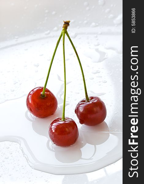 Three cherries lay on a plate and are reflected in drops of water. Three cherries lay on a plate and are reflected in drops of water