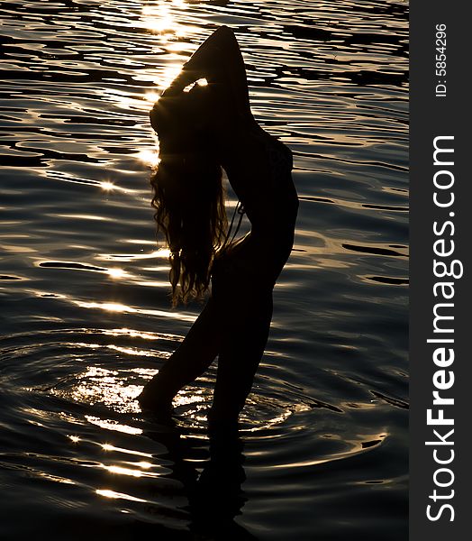 Beautiful silhouette of the girl on a background of water with the reflected sun on a decline