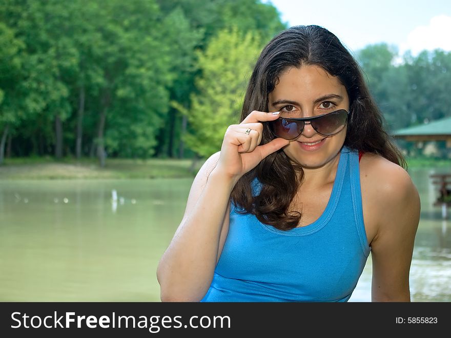 A beautiful girl, wearing sunglasses, sitting on a bench near a lake, smiling. A beautiful girl, wearing sunglasses, sitting on a bench near a lake, smiling