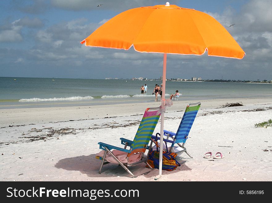 A bright beach umbrella poised over two empty sun chairs. A bright beach umbrella poised over two empty sun chairs