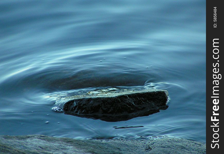 Rock at edge of lake with ripples of metallic blue water. Rock at edge of lake with ripples of metallic blue water.