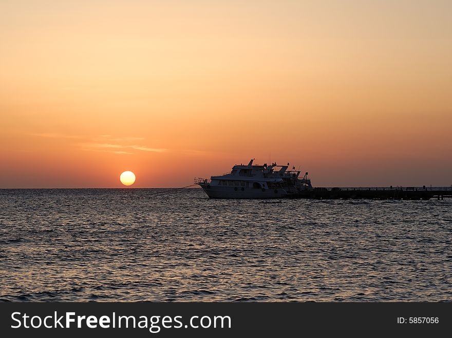 Sunrise on the sea with a yacht in foreground.