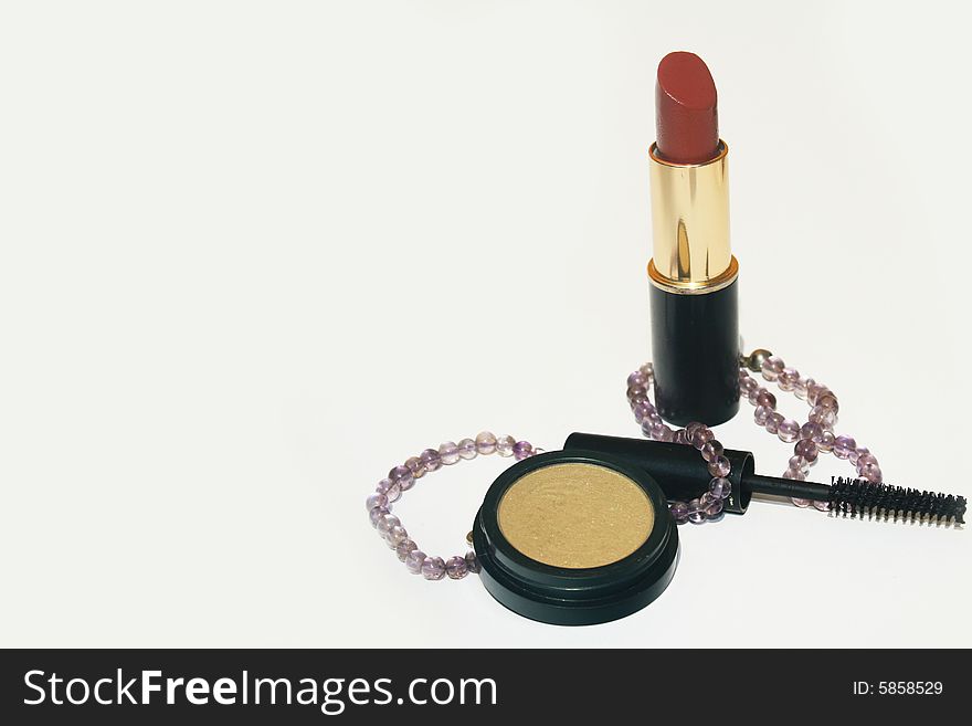 Lipstick, mascara, eyeshadow and a necklace on white background with copy space on left. Lipstick, mascara, eyeshadow and a necklace on white background with copy space on left