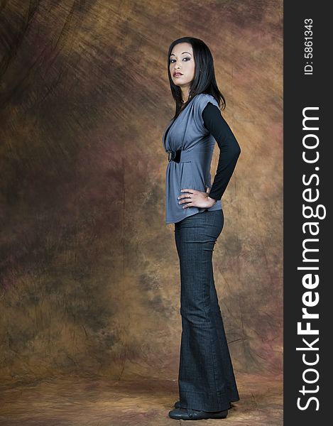 Full length image of a dark haired lady in a blue blouse and denims standing side on with hands on hips. Full length image of a dark haired lady in a blue blouse and denims standing side on with hands on hips.