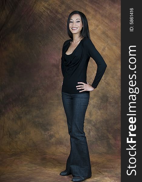 Full length image of a dark haired lady in a blue blouse and denims standing side on with hands on hips and smiling. Full length image of a dark haired lady in a blue blouse and denims standing side on with hands on hips and smiling.