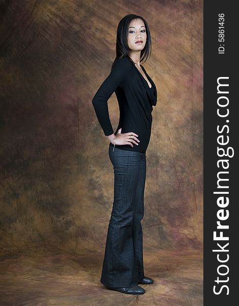 Full length image of a dark haired lady in a blue blouse and denims standing side on facing right with hands on hips and smiling. Full length image of a dark haired lady in a blue blouse and denims standing side on facing right with hands on hips and smiling.