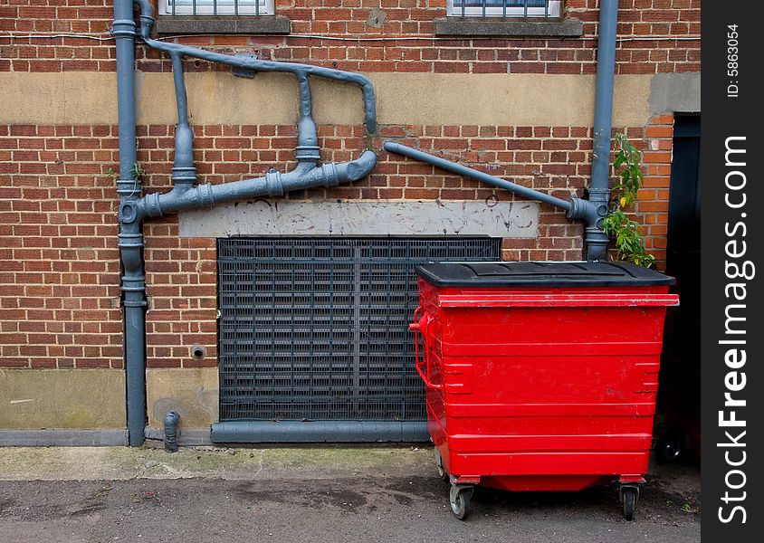 Sewer pipes outside the old brick house and bright red waste container near the wall. Sewer pipes outside the old brick house and bright red waste container near the wall