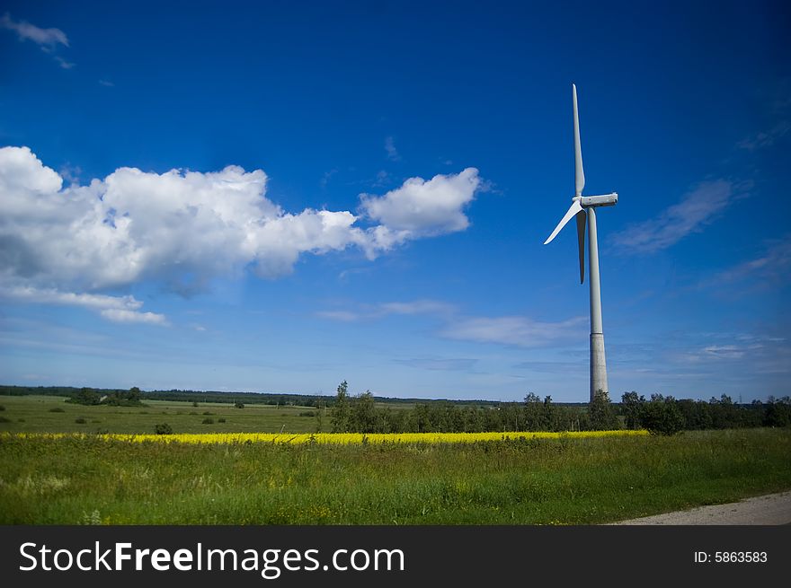 Windmill with green field and blue sky with clouds.