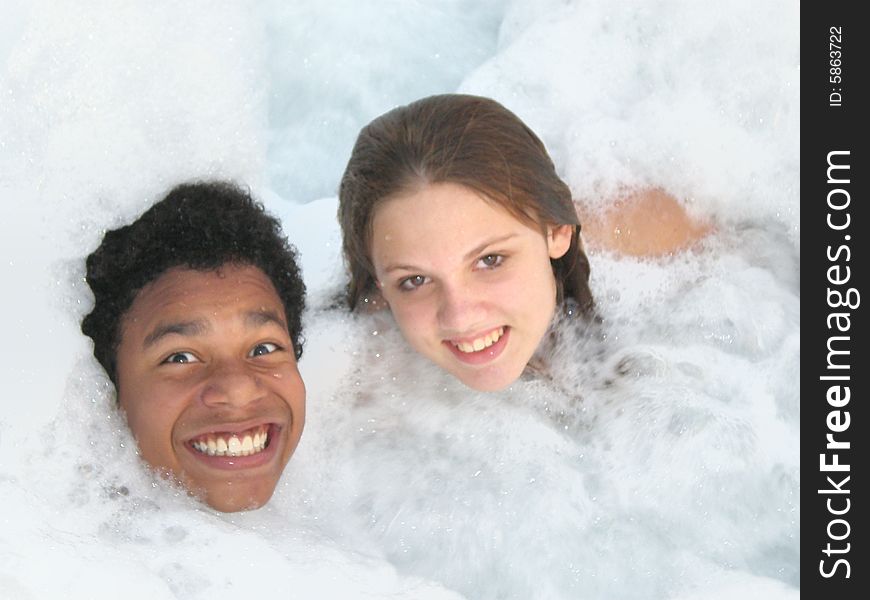 A picture of a black boy and a white girl smiling in a jacuzzi with lots of bubbles. A picture of a black boy and a white girl smiling in a jacuzzi with lots of bubbles.