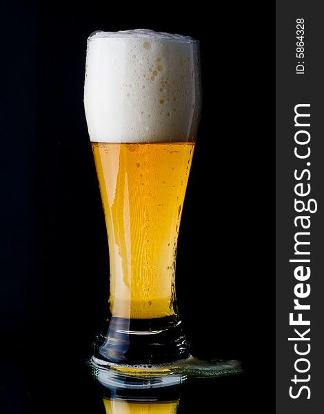 Fresh foamy beer in a glass on a black background.
