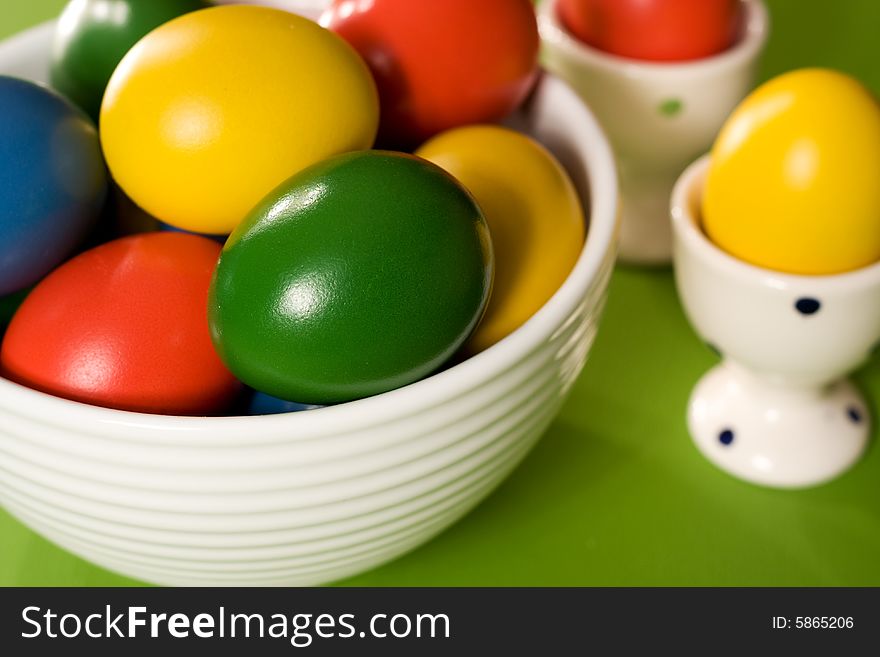 Colorful Easter Eggs in white bowl on green background