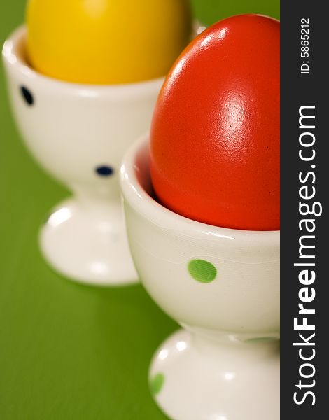 Yellow and red Easter Eggs in white bowl on green background