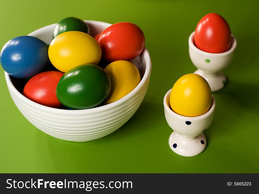 Colorful Easter Eggs in white bowl on green background