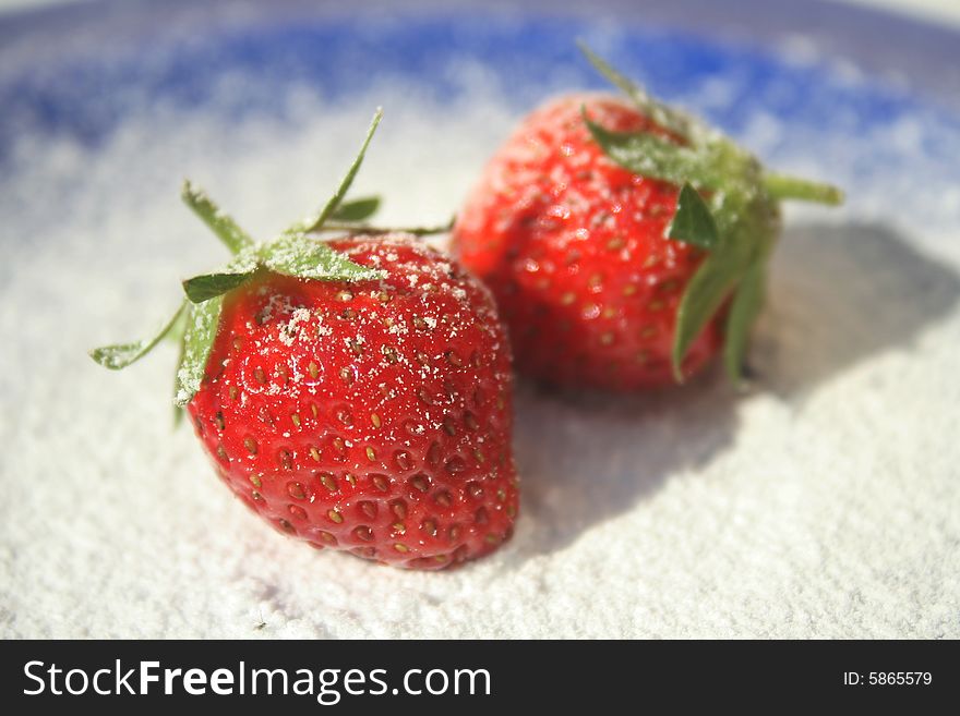 Two ripe red strawberries on blue plate with powered sugar sprinkled on them. Two ripe red strawberries on blue plate with powered sugar sprinkled on them