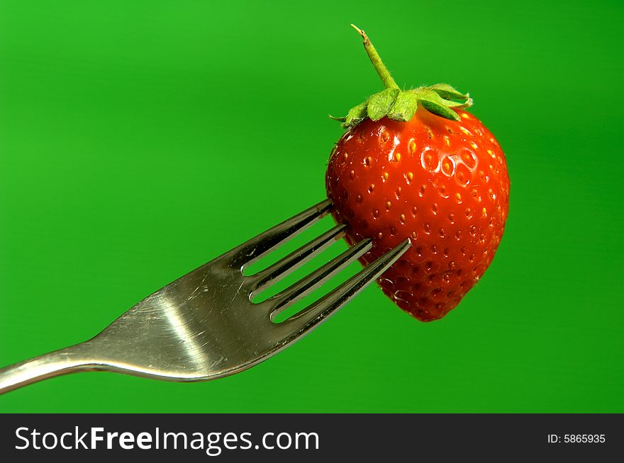 One strawberry on fork on green background. One strawberry on fork on green background