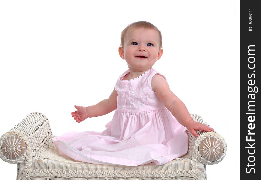 Smiling baby girl on wicker bench, wearing pink dress