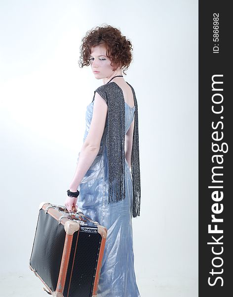 A young girl with a curly hair, dressed in the outmoded clothes, holds an old suitcase in a hand and looks a sorrowful look through a shoulder. A young girl with a curly hair, dressed in the outmoded clothes, holds an old suitcase in a hand and looks a sorrowful look through a shoulder